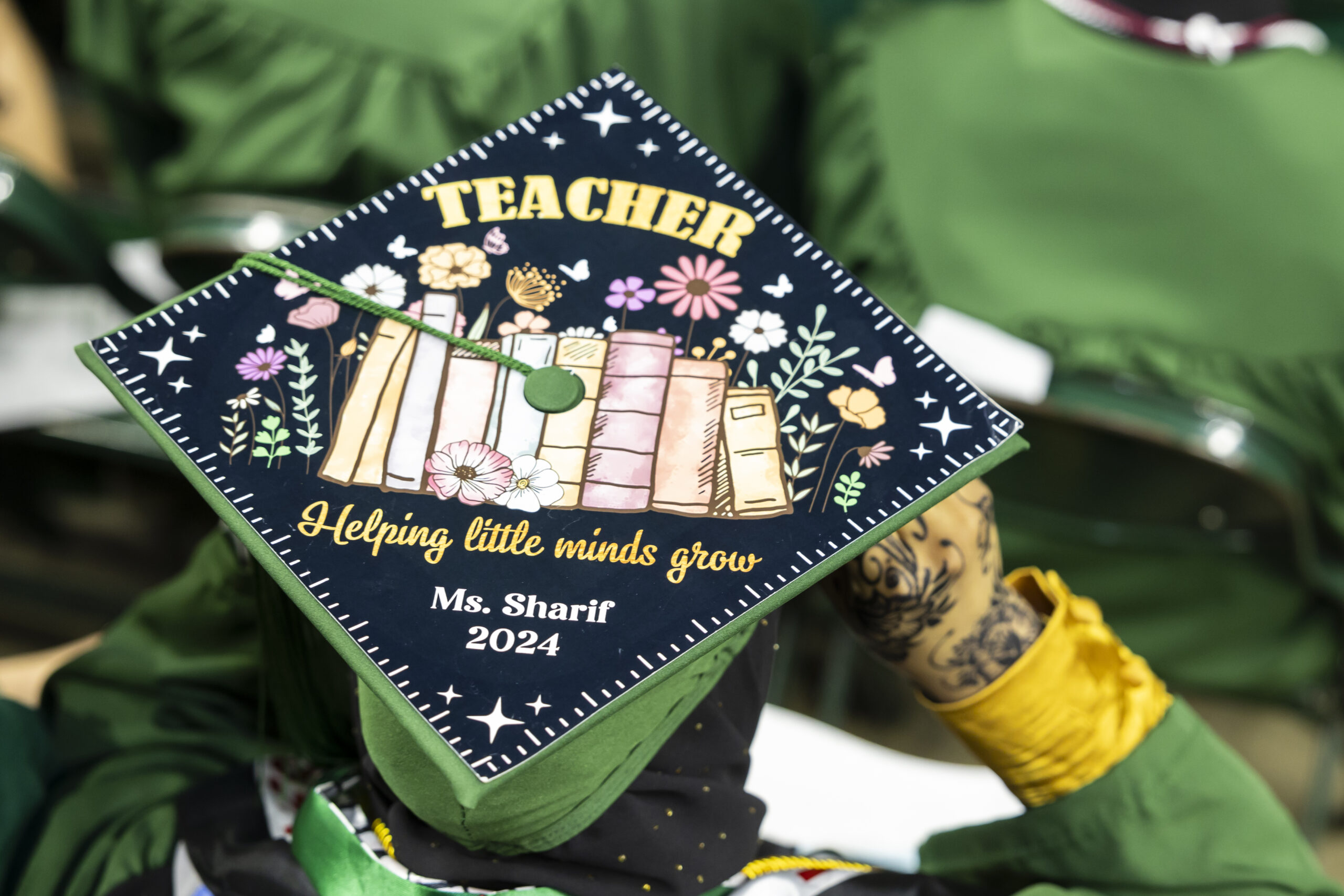 George Mason graduate wearing a grad cap decorated to say "Teacher: helping little minds grow"